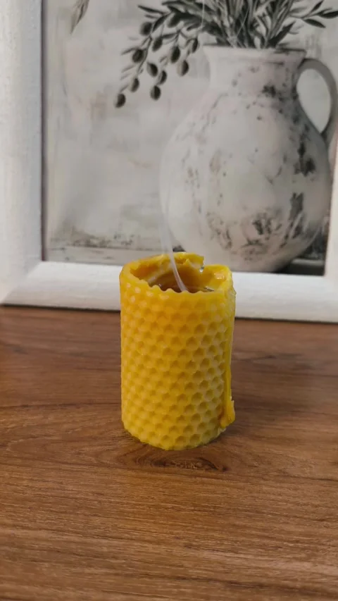 Handmade beeswax candle with honeycomb texture smoking on wooden table Stock Footage 340356946