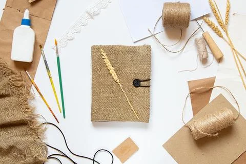 A handmade burlap notebook lies on a white background among papers and thread Stock Photos