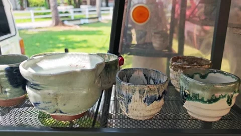 Handmade ceramic cups and pottery on a display shelf. Видео 340506702