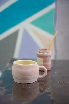 Handmade ceramic mug covered with pink glaze standing on pottery workshop table Stock Photos