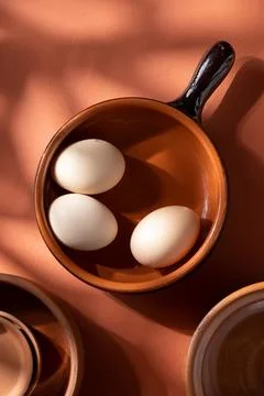 Handmade ceramic plates with home eggs on brown background. Terracotta objects,  Stock Photos