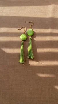 Handmade earrings with green elements resting on a fabric surface under lig.. Stock Photos