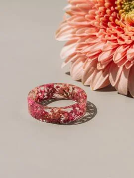 Handmade epoxy resin ring with pink dried flowers beside blossom on neutral Stock Photos