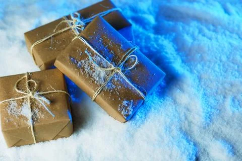 Handmade gift boxes from craft paper over snowy wooden table in blue light. Stock Photos