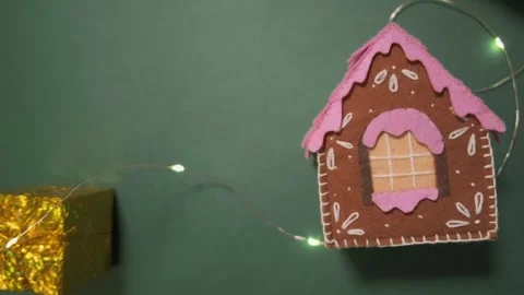 Handmade gingerbread house with pink icing and a gold gift box on a green Stock Footage 319413580