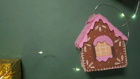 Handmade gingerbread house with pink icing and a gold gift box on a green Stock Footage 319894923