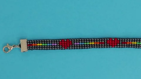 Handmade LGBT bead pattern necklace over turquoise background. Close up Stock Footage 267814995