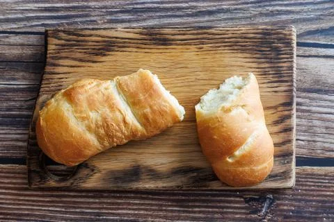Handmade long loaf bread broken off on wooden cutting board against dark wooden Stock Photos