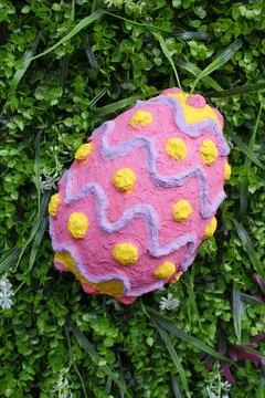 Handmade pink Easter egg with yellow dots resting on green grass Stock Photos