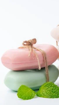 Handmade soap sits on a white surface with fresh mint leaves nearby in a simple Stock Photos