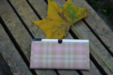 Handmade wallet and yellow leaf on a wooden bench Stock Photos