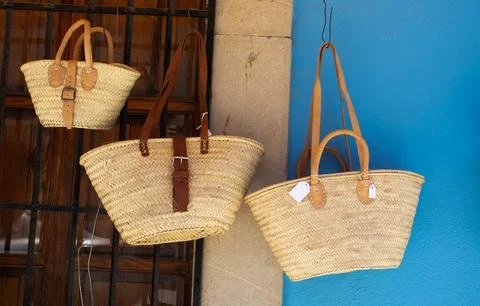 Handmade wicker baskets with leather straps hanging against a rustic wooden.. Stock Photos
