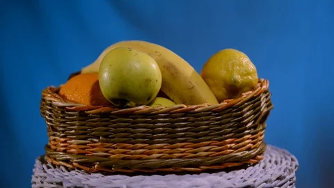 Handmade wicker fruit basket: orange, banana, apples - move on blue background Stock Footage 114968302