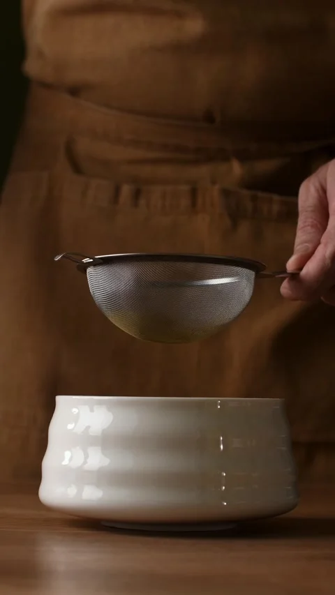 Hands add roasted hojicha powder to fine mesh sieve and sift it into ceramic Video stock 340874614
