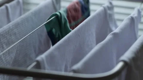 Hands Adding Colored T-Shirt to Drying Rack with White Children’s Tank Tops Stock Footage 321831378