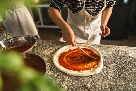 Hands adding fresh tomato sauce to pizza dough. Pizza ingredients on the wooden Stock Photos