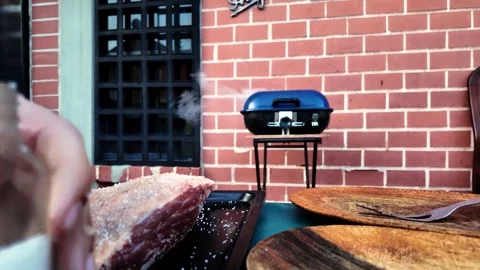 Hands adding salt to raw meat for barbecue on backyard grill - BBQ season Stock Footage 316234099