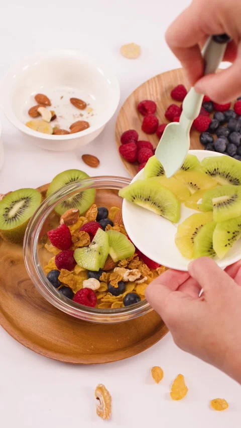 Hands Adding Sliced Kiwi to a Healthy Breakfast Cereal Bowl Stock Footage 337533268