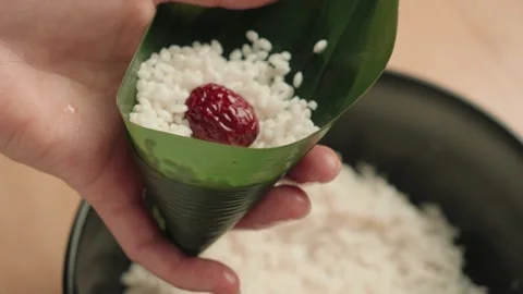 Hands Adding Sticky Rice to Bamboo Leaf Cone for Traditional Dumplings Видео 339070008