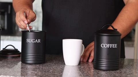 Hands adding sugar to a cup of coffee on a kitchen countertop, illustrating.. Stock Footage 301420478