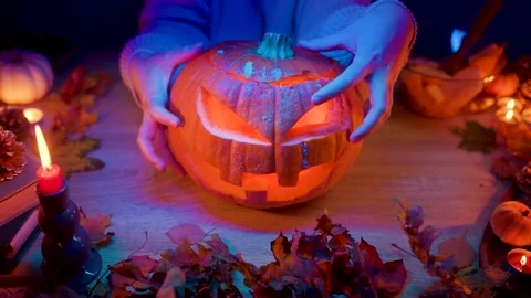 Hands adjust a glowing carved pumpkin lantern during Halloween preparation at ho Stock Footage 345685387