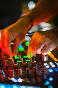 Hands adjust knobs and faders on a DJ mixer during a night event in a busy cl Stock Photos