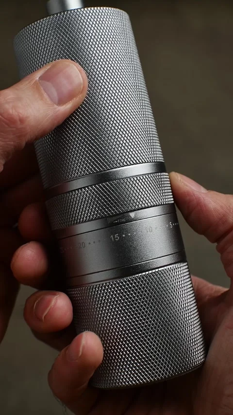 Hands adjust the numbered grind setting ring on a metal manual coffee grinder in Stock Footage 346743605