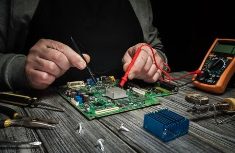 Hands adjust wires while testing a circuit board using a multimeter. Tools ar Stock Photos