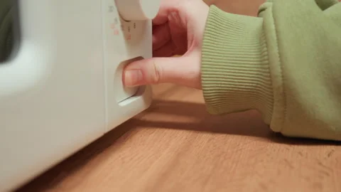 Hands adjusting microwave control knob on white appliance beside wooden Stock-Footage 345654192