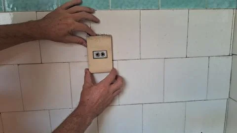 Hands adjusting an old electrical wall outlet on tiled surface Stock Photos