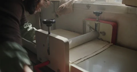 Hands adjusting a slab roller while flattening clay in a sunlit ceramic studio Stock Footage 302554020