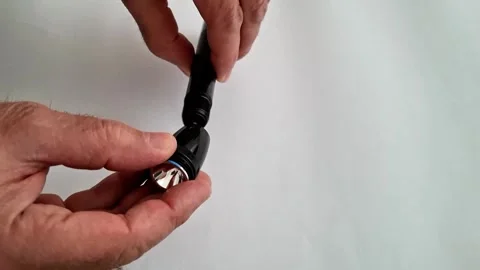 Hands Adjusting Small Black Flashlight with Blue Ring on White Background 動画素材 332890595