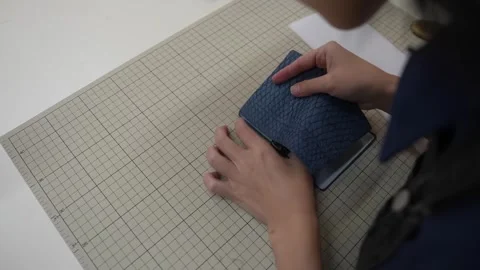 Hands align trimmed leather panel against paper pattern piece Stock Footage 339966905