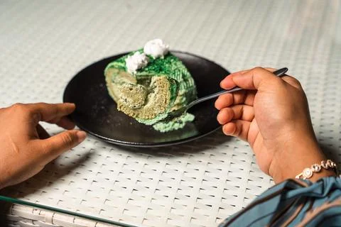 Hands and a fork cut into a slice of green pandan cake roll on a black plate. Foto stock