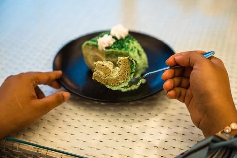 Hands and a fork cut into a slice of green pandan cake roll on a black plate. Foto stock