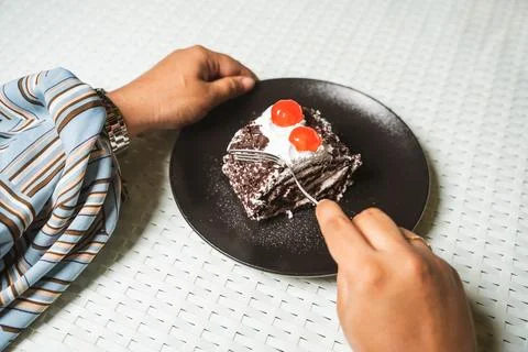 Hands and a fork cut into a slice of black forest cake roll with cream and ch Foto stock