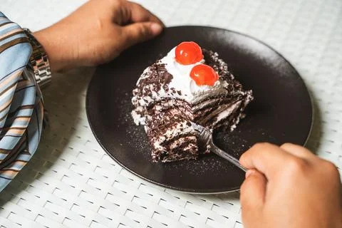 Hands and a fork cut into a slice of black forest cake roll with cream and ch Foto stock