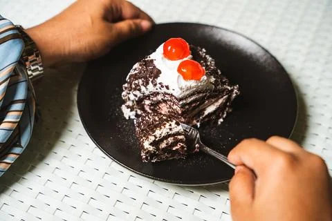 Hands and a fork cut into a slice of black forest cake roll with cream and ch Foto stock