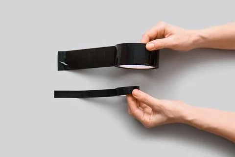 Hands applying black electrical tape and duct tape on gray background for rep Stock Photos