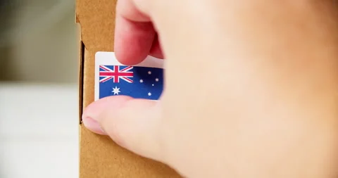 Hands applying MADE IN AUSTRALIA flag label on a shipping cardboard box Stock Footage 199062049