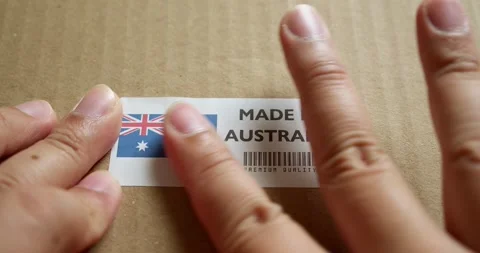 Hands applying MADE IN AUSTRALIA flag label on a shipping box with product Stock Footage 254079040
