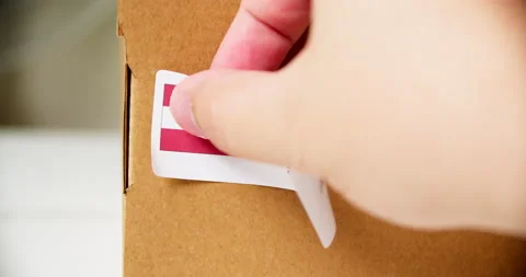 Hands applying MADE IN AUSTRIA flag label on a shipping cardboard box with Stock Footage 201111958