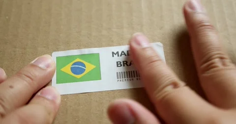 Hands applying MADE IN BRAZIL flag label on a shipping box with product Stock Footage 254086978