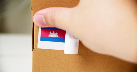 Hands applying MADE IN CAMBODIA flag label on a shipping cardboard box Stock Footage 199655988