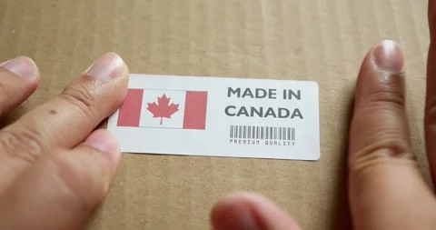 Hands applying MADE IN CANADA  flag label on a shipping box with product Stock Footage 253383489