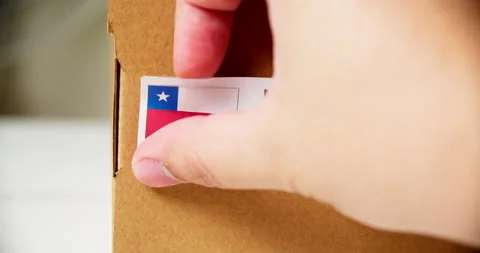 Hands applying MADE IN CHILE flag label on a shipping cardboard box with Stock Footage 200831326