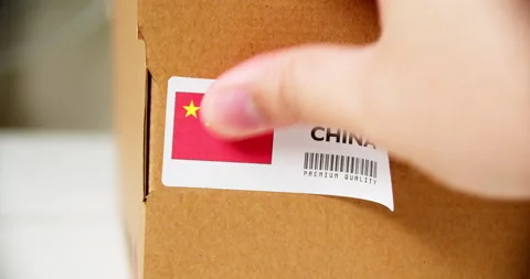 Hands applying MADE IN CHINA flag label on a shipping cardboard box with Stock Footage 199009123