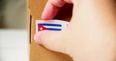Hands applying MADE IN CUBA flag label on a shipping cardboard box with Stock Footage 201111875