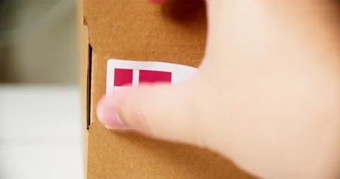 Hands applying MADE IN DENMARK flag label on a shipping cardboard box with Stock Footage 199459897