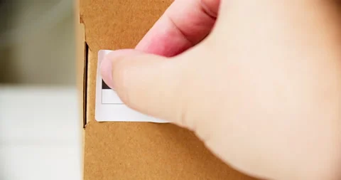 Hands applying MADE IN ESTONIA flag label on a shipping cardboard box with Stock Footage 201111942